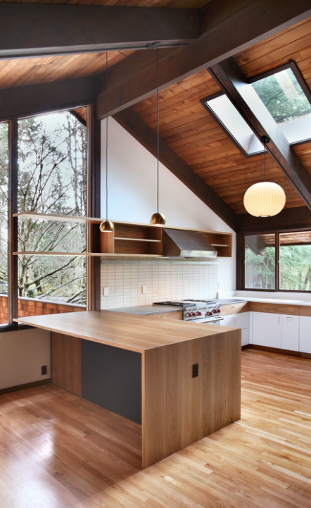 Kitchen with white walls and stainless steel appliances along with hardwood floors, island and shelving lighted by pendant lights.
