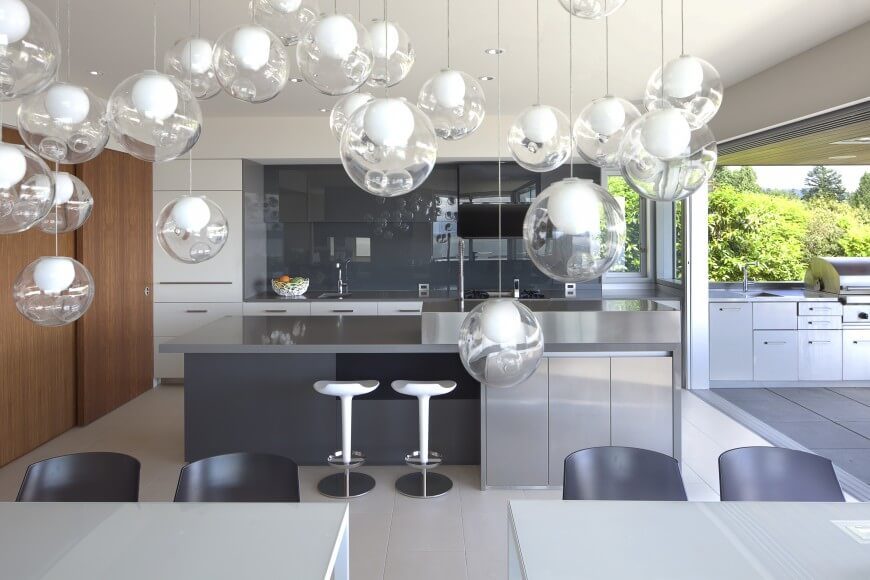 Modern kitchen with smooth solid countertops and a gray backsplash styled by multiple pendant lights.
