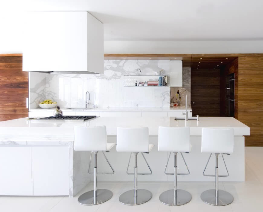 Kitchen with marble backsplash and smooth white countertops along with a large center island featuring a breakfast bar.