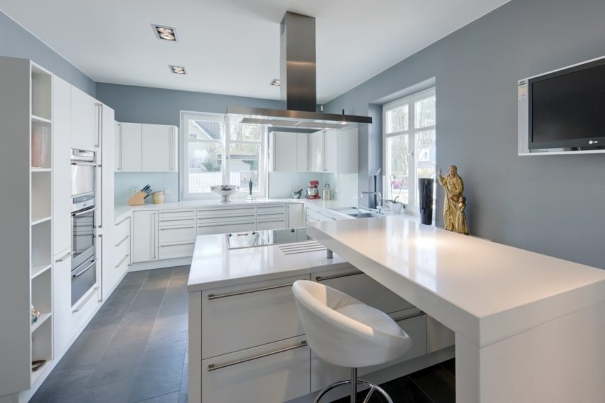Modern kitchen with gray walls and white cabinetry along with smooth white countertops and center island with a built-in desk.