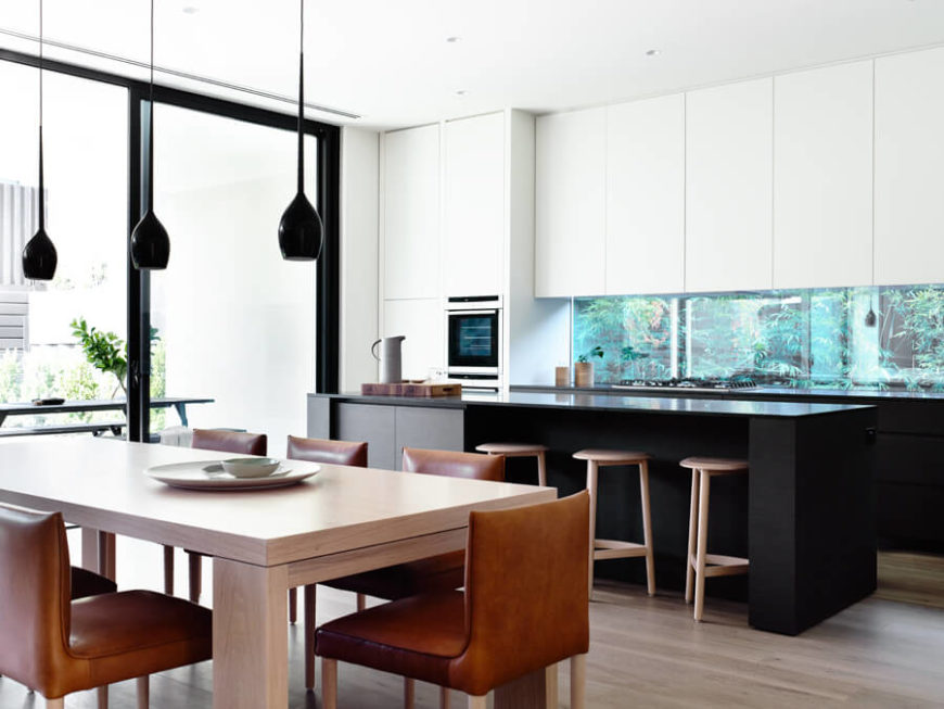 Contemporary kitchen with white walls and cabinetry along with black countertops and a center island featuring a breakfast bar and a dine-in table set.