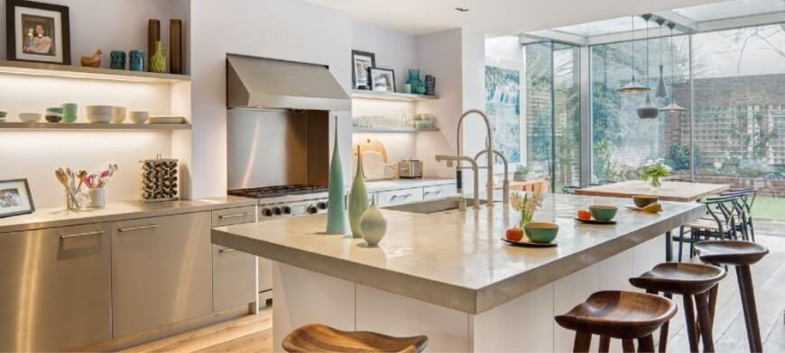Bright, open design informs this modern kitchen, centered on a large white island with an extended countertop for dining space. A set of carved wood bar stools act as a rustic counterpoint to the contemporary look of stainless steel appliances and cupboard doors. Bright, open design informs this modern kitchen, centered on a large white island with an extended countertop for dining space. A set of carved wood bar stools act as a rustic counterpoint to the contemporary look of stainless steel appliances and cupboard doors.
