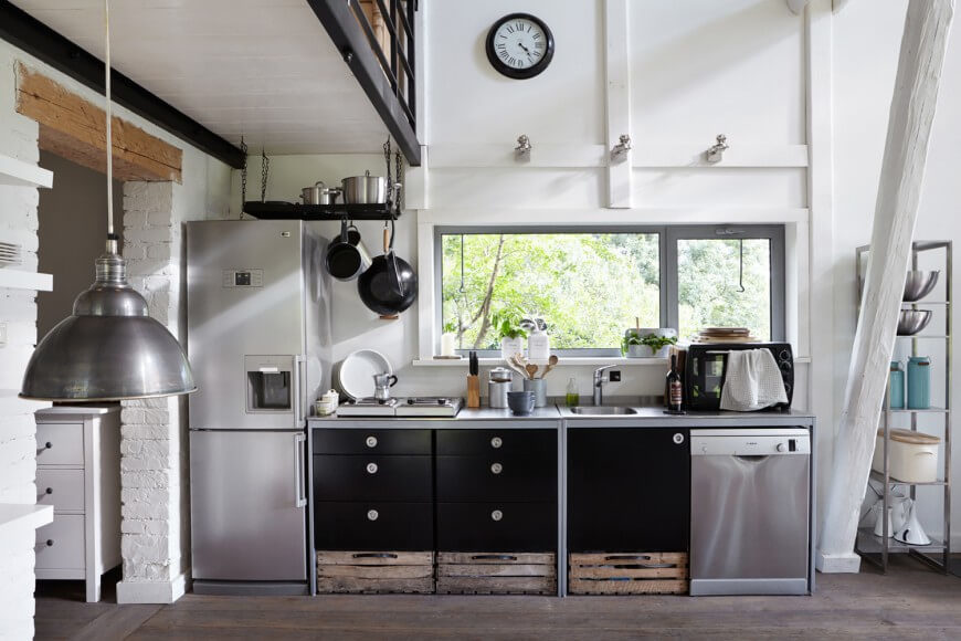As part of a much larger open space, the kitchen here is defined by its stainless steel appliances. A set of black cabinetry contrasts with white walls and rustic storage bins below. As part of a much larger open space, the kitchen here is defined by its stainless steel appliances. A set of black cabinetry contrasts with white walls and rustic storage bins below.