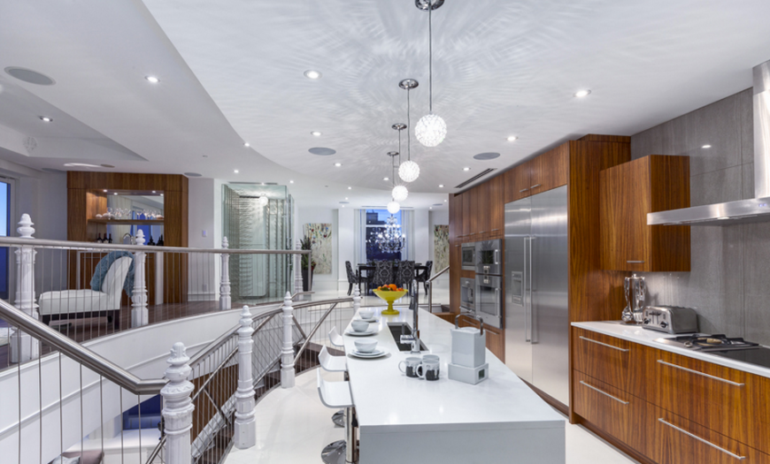 This kitchen is an absolute riot of color and texture, with bright natural wood cabinetry holding stainless steel appliances at right, and a pristine white island at center. Within a larger open design area, the kitchen is defined by this high contrast look. This kitchen is an absolute riot of color and texture, with bright natural wood cabinetry holding stainless steel appliances at right, and a pristine white island at center. Within a larger open design area, the kitchen is defined by this high contrast look.