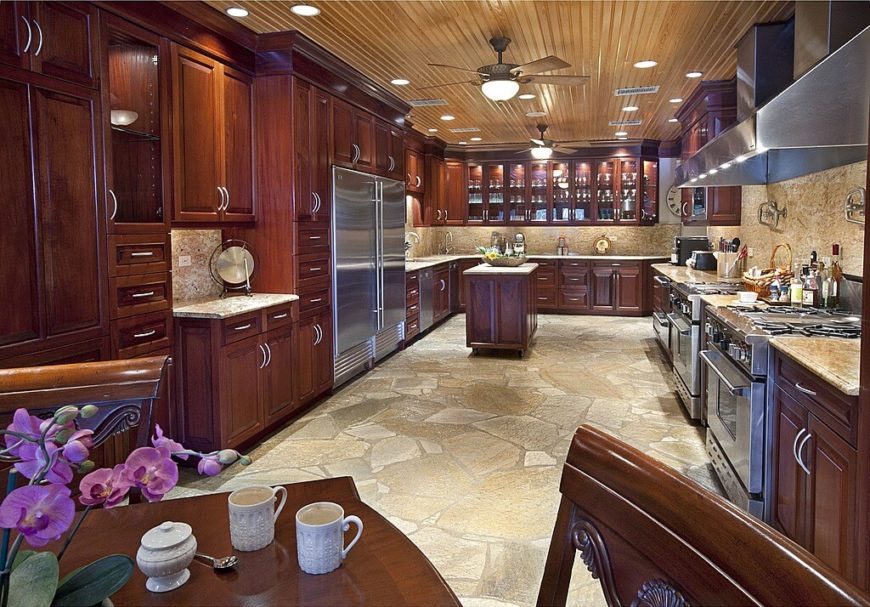 This vast kitchen features acres of rich wood cabinetry, plus marble countertops and backsplash over a stone floor. The ceiling features sleek wood planks and the intricate lighting scheme highlights the array of stainless steel appliances throughout. This vast kitchen features acres of rich wood cabinetry, plus marble countertops and backsplash over a stone floor. The ceiling features sleek wood planks and the intricate lighting scheme highlights the array of stainless steel appliances throughout.
