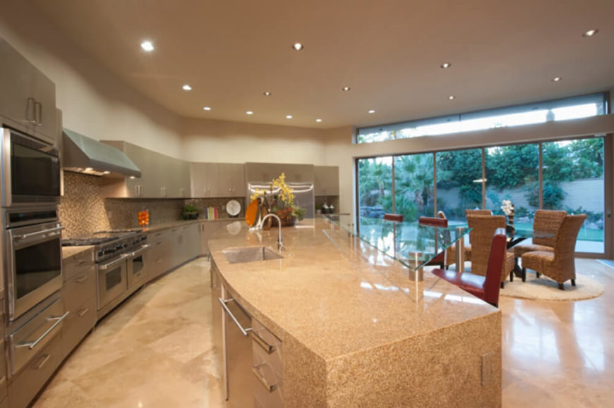 Here's an enormous open plan kitchen design, lit naturally through a row of full height windows. The giant granite wrapped island at center defines the space, in contrast with both sleek grey cabinetry and stainless steel appliances dotting the space. Here's an enormous open plan kitchen design, lit naturally through a row of full height windows. The giant granite wrapped island at center defines the space, in contrast with both sleek grey cabinetry and stainless steel appliances dotting the space.
