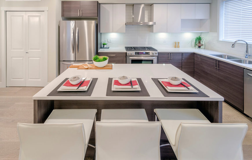 Ultra modern minimalism informs this sleek kitchen, pairing white countertops, tile backsplash, and upper cabinets with rich wood lower cupboards and island. The stainless steel appliances add a small dose of contrast. Ultra modern minimalism informs this sleek kitchen, pairing white countertops, tile backsplash, and upper cabinets with rich wood lower cupboards and island. The stainless steel appliances add a small dose of contrast.