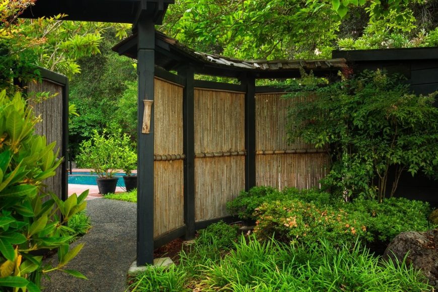 A curved fence with lacquered black supports has a large gate that opens up to expose the backyard, complete with a beautiful aqua pool. The forested lot has plants growing right up to the fence, embracing the natural look favored by Japanese gardens. A curved fence with lacquered black supports has a large gate that opens up to expose the backyard, complete with a beautiful aqua pool. The forested lot has plants growing right up to the fence, embracing the natural look favored by Japanese gardens.