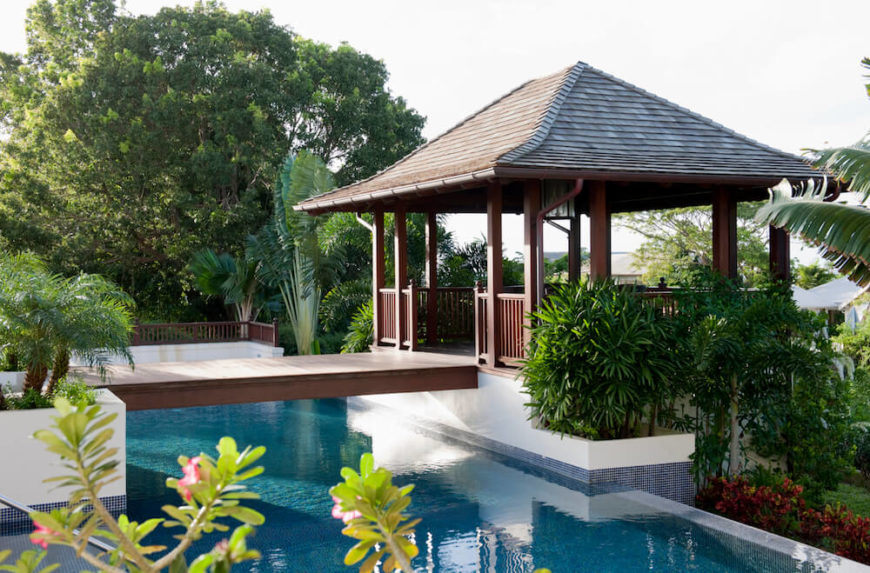 A poolside gazebo attached to the main concrete patio by means of a simple wooden foot bridge with no railings. The property is surrounded by tropical flora and overlooks the sea. A poolside gazebo attached to the main concrete patio by means of a simple wooden foot bridge with no railings. The property is surrounded by tropical flora and overlooks the sea.