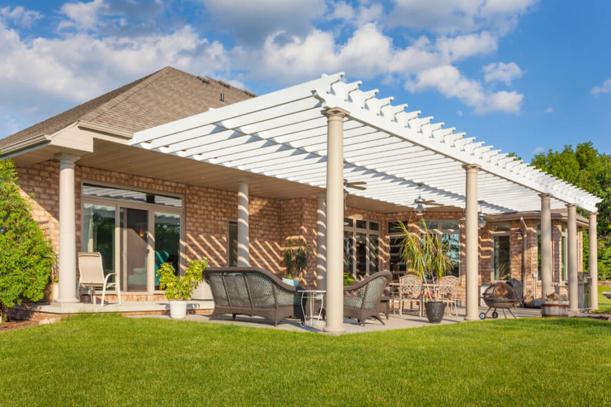 This large pergola is attached to the narrow back veranda and extends over a larger patio area. This pergola adds a bit of grandiose style to this patio, drawing the eye upwards. This large pergola is attached to the narrow back veranda and extends over a larger patio area. This pergola adds a bit of grandiose style to this patio, drawing the eye upwards.