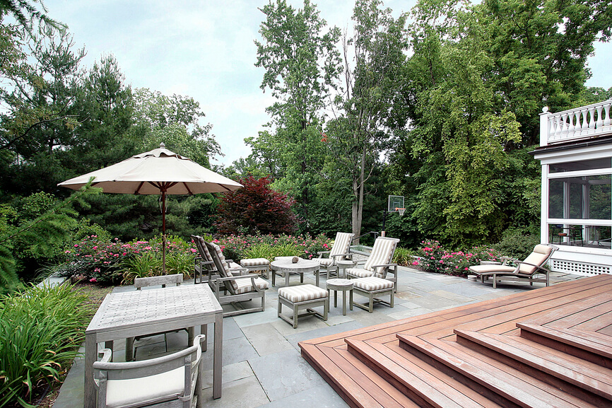 A large open patio tucked into a private garden. Steps lead down from the wooden deck. The outdoor patio complete with plenty of seating is overlooked by a balcony and screened-in sunroom. A large open patio tucked into a private garden. Steps lead down from the wooden deck. The outdoor patio complete with plenty of seating is overlooked by a balcony and screened-in sunroom.