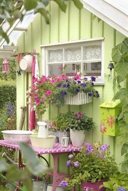 An adorable spring-green garden shed decked out with lots of containers of flowers and gardening accessories. A small pink table rests against one outer wall, a great workstation! An adorable spring-green garden shed decked out with lots of containers of flowers and gardening accessories. A small pink table rests against one outer wall, a great workstation!