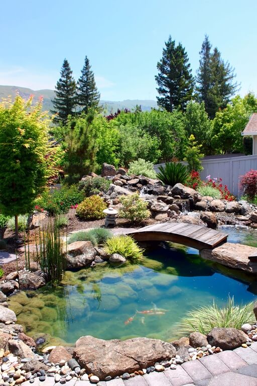A small wooden footbridge connecting the flagstone pathway to a small stone outcropping. The bridge expands over a small koi pond in a Japanese Zen garden. 30z-backyard-pillar-post-bridges A small wooden footbridge connecting the flagstone pathway to a small stone outcropping. The bridge expands over a small koi pond in a Japanese Zen garden.