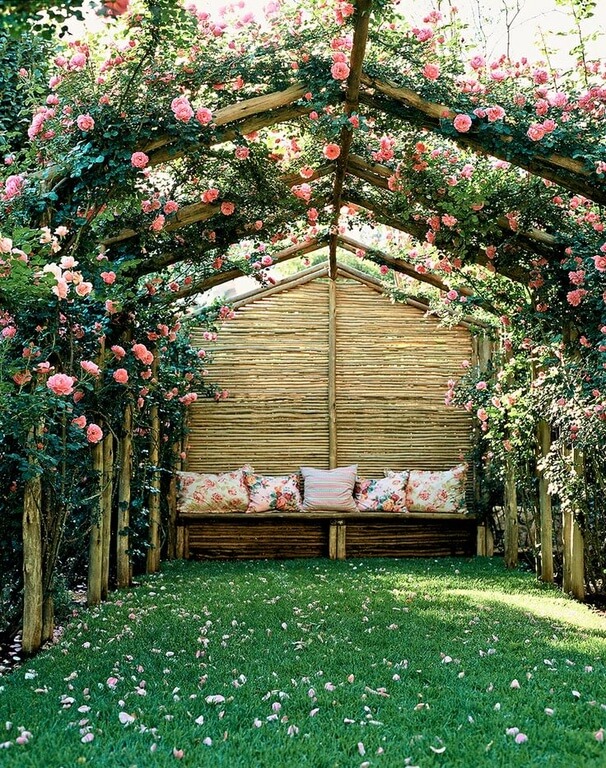This tall trellis structure creates a tunnel of light pink roses that form a blanket above the small seating area to the rear of the tunnel. This tall trellis structure creates a tunnel of light pink roses that form a blanket above the small seating area to the rear of the tunnel.