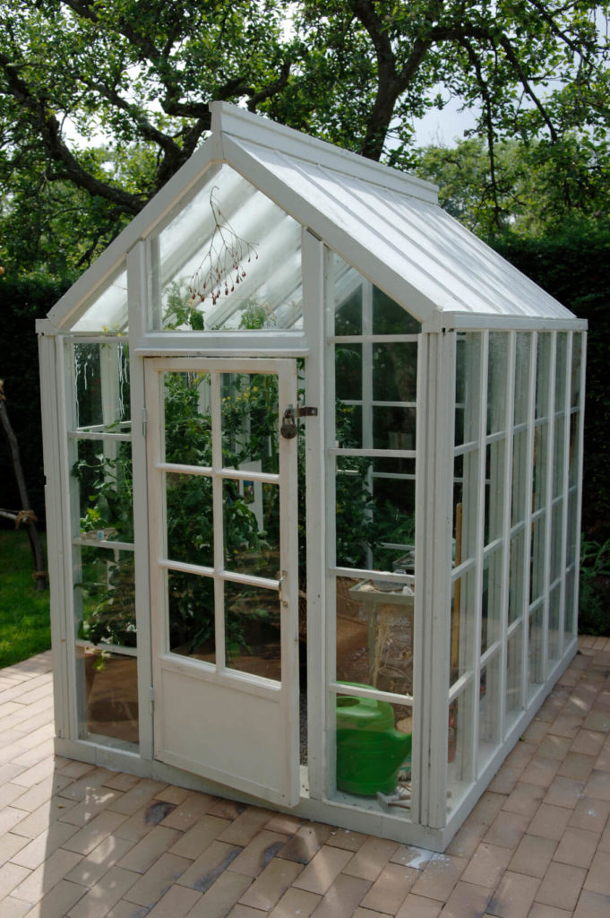A small white greenhouse the doubles as a gardening shed. This structure is placed upon the brick patio. A small white greenhouse the doubles as a gardening shed. This structure is placed upon the brick patio.