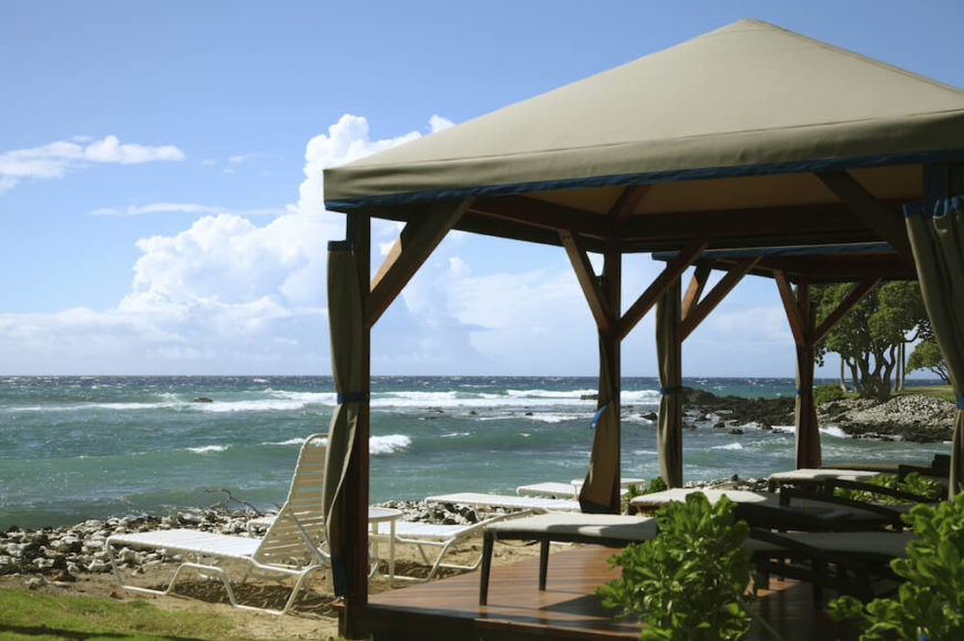 A beachside pavilion with lots of lounge chairs beneath. The rocky shores lead into the pounding surf. A beachside pavilion with lots of lounge chairs beneath. The rocky shores lead into the pounding surf.