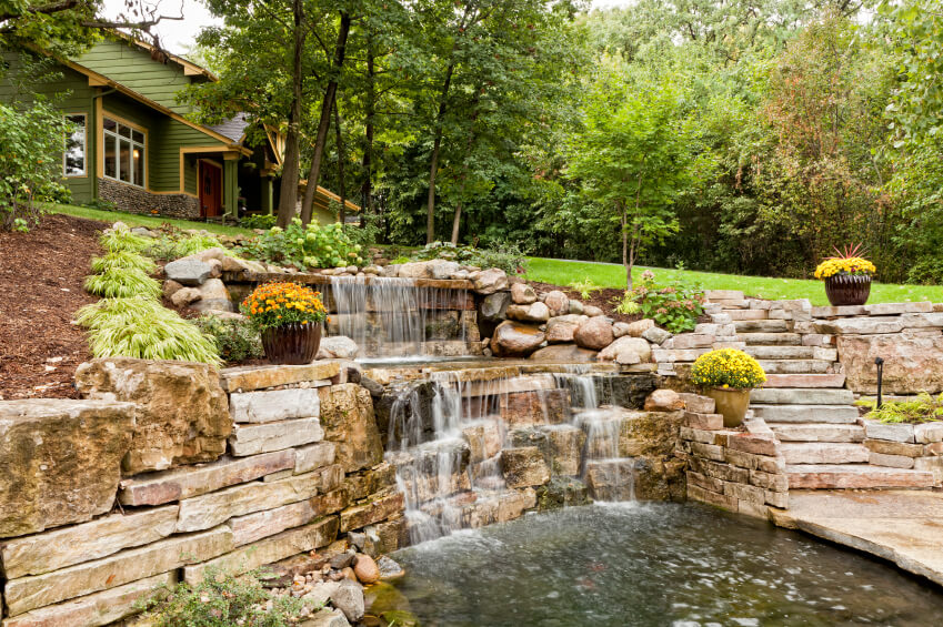 A massive backyard waterfall that leads down from the main yard to a lower patio that is surrounded by water. A massive backyard waterfall that leads down from the main yard to a lower patio that is surrounded by water.