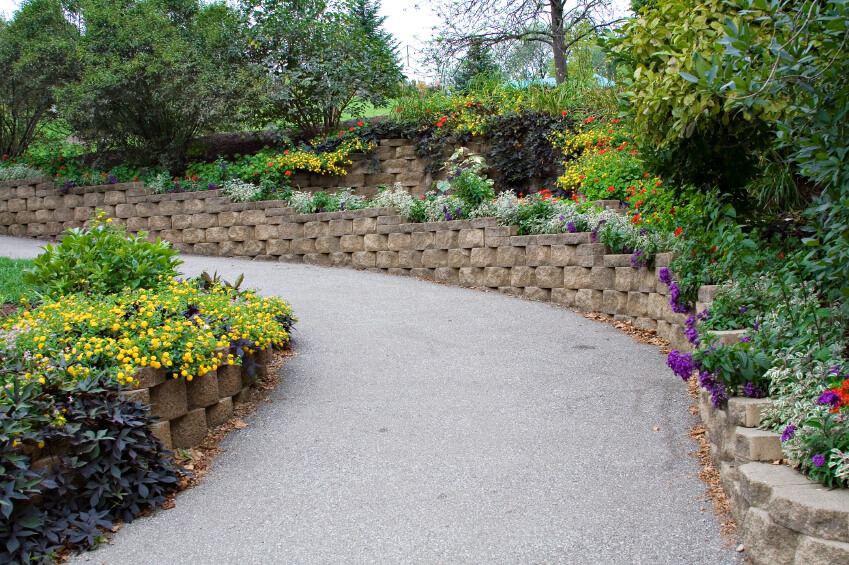 This winding retaining wall is made out of stacked stone bricks and is decorated with flowers and plants all the way up. This winding retaining wall is made out of stacked stone bricks and is decorated with flowers and plants all the way up.