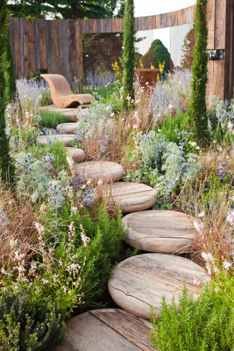 These smooth, rustic stepping stones carve a pathway through dense ground cover landscaping to a patio. These smooth, rustic stepping stones carve a pathway through dense ground cover landscaping to a patio.