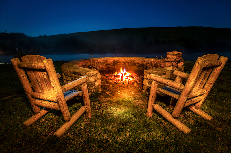 This fire pit is unusual in that it is partially open on one side, which isn't recommended. Two sturdy rustic chairs are positioned on this side, overlooking the view of the lake. This fire pit is unusual in that it is partially open on one side, which isn't recommended. Two sturdy rustic chairs are positioned on this side, overlooking the view of the lake.