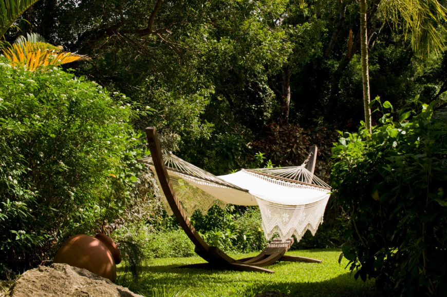 This lovely crocheted hammock is strung between the two ends of a half-circle wooden stand. The hammock sits in a secluded part of the yard amongst the trees. This lovely crocheted hammock is strung between the two ends of a half-circle wooden stand. The hammock sits in a secluded part of the yard amongst the trees.