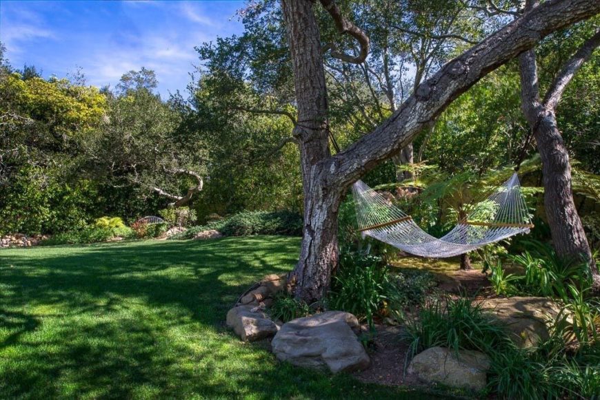This hammock is strung between two mature trees in the middle of a planting bed marked by rocks. This hammock is strung between two mature trees in the middle of a planting bed marked by rocks.