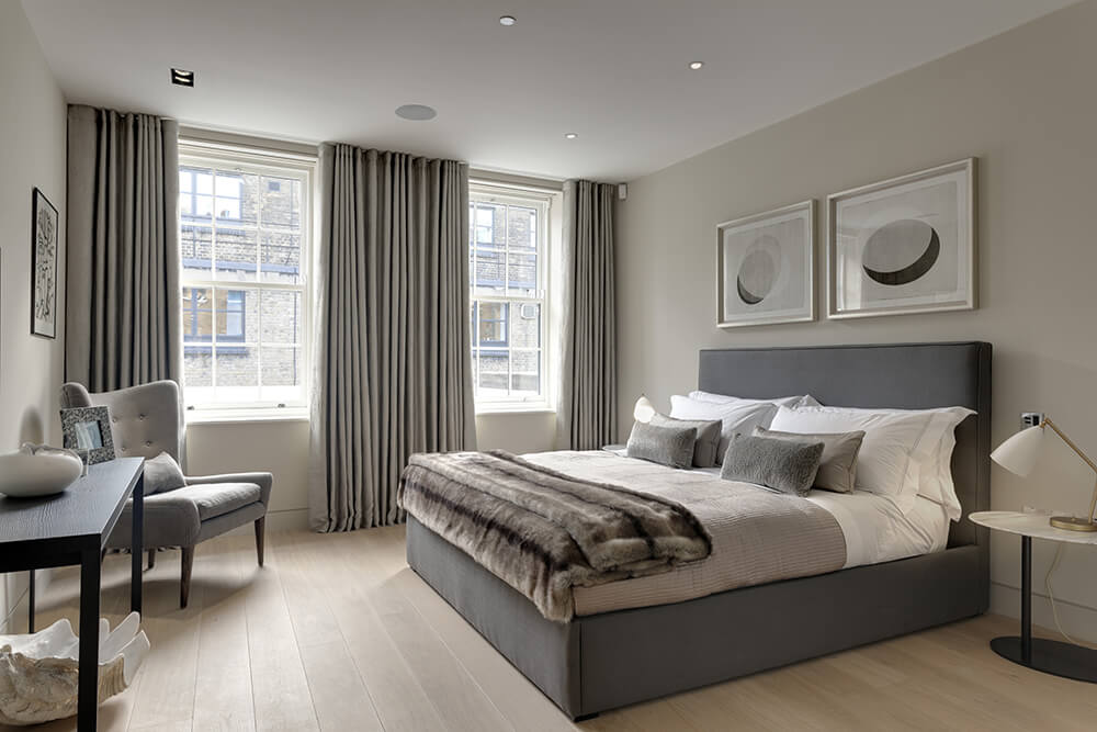 Medium-sized primary bedroom featuring hardwood flooring and gray walls matching the gray window curtains and gray bed frame.