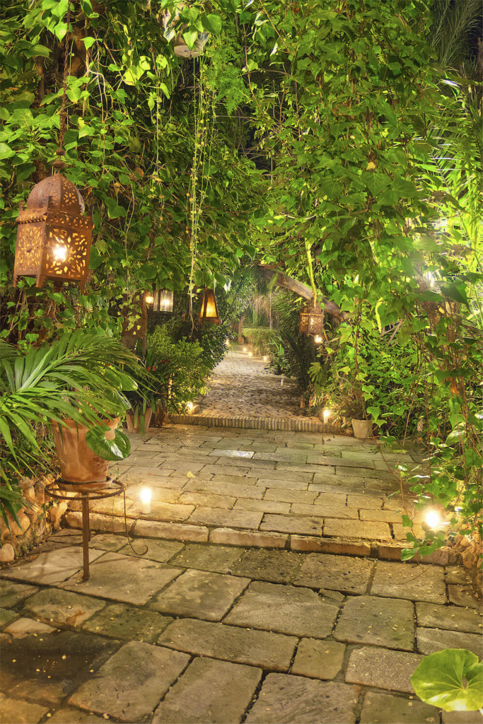 Here is an interesting idea where fixtures are placed on the ground but left as standard light bulbs without shades or adornments. There are also rust colored lanterns hanging around the garden. This look has an industrial appeal, hearkening back to the era of steam.