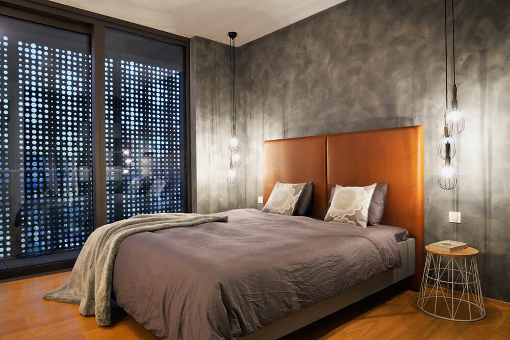 A magnificent primary bedroom with a large bed set on the hardwood flooring. The room has gray walls and a stunning pendant lighting.