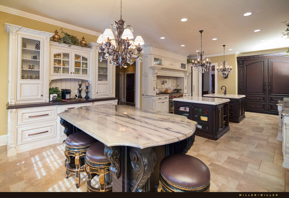 This kitchen offers 3 islands, one serving as the breakfast bar. All the islands are lighted by fancy chandeliers set on a regular ceiling.
