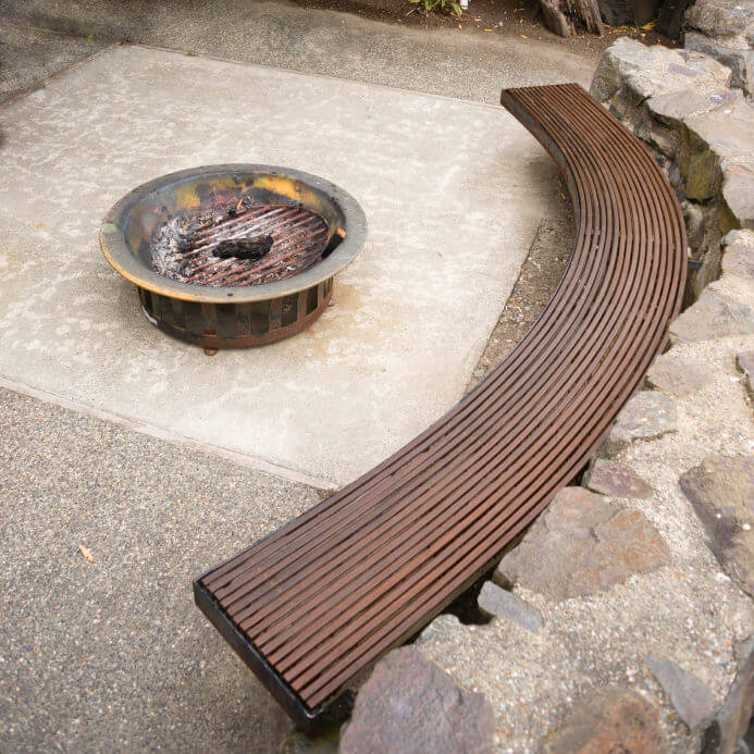 Round grate style fire pit on concrete slab patio with curved would bench seating. Round grate style fire pit on concrete slab patio with curved would bench seating.