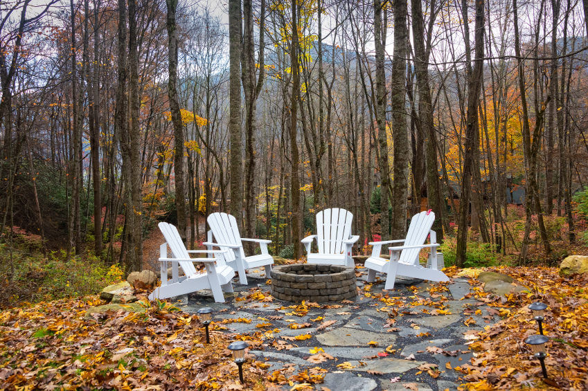 Flagstone Forest patio with brick round fire pit surrounded by striking white Adirondack chairs. Flagstone Forest patio with brick round fire pit surrounded by striking white Adirondack chairs.