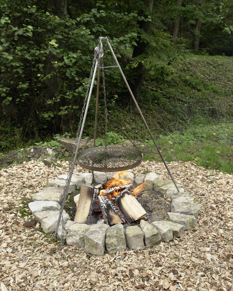A very simple round fire pit created with rocks includes a hanging cooking grate suspended from teepee structure. A very simple round fire pit created with rocks includes a hanging cooking grate suspended from teepee structure.