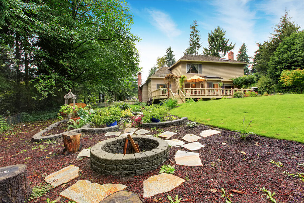 Round wood-burning fire pit placed an a large garden in the backyard. Round wood-burning fire pit placed an a large garden in the backyard.