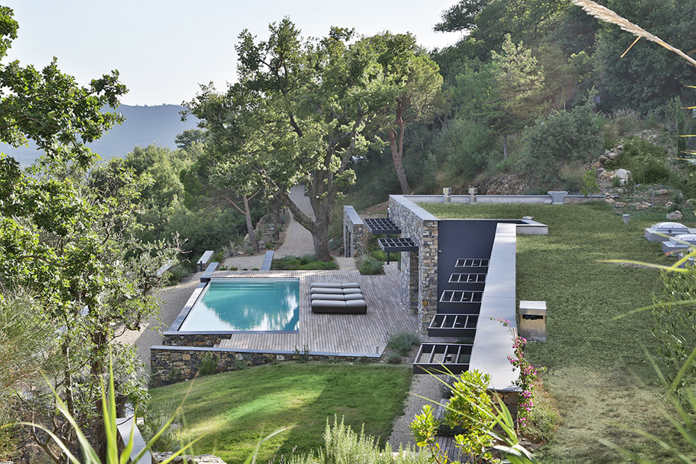 Aerial view of this modern home's pool area surrounded by the home's deck. It also features multiple lounger seats.