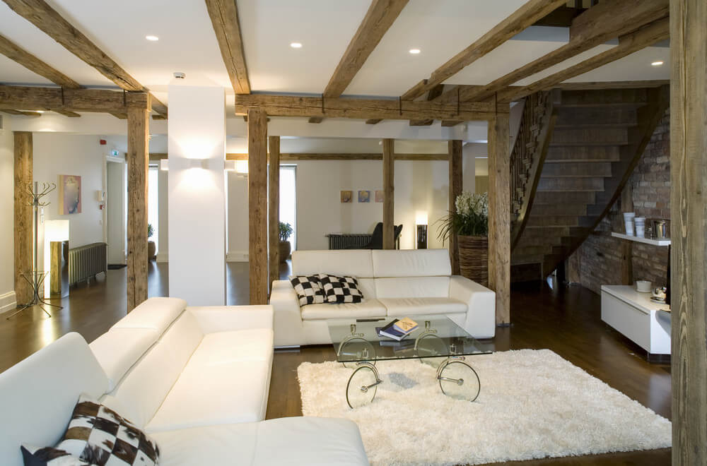 Use lighter blends of grey, white and browns for your living room if your living room combines wood and marble materials for your walls and accents. Use white paint for your walls and ceilings and allow browns and greys to accentuate the fixtures and other parts of your room like the stairs and house foundations. This living room offers rustic pillars and hardwood floors, as well as a ceiling with exposed beams.