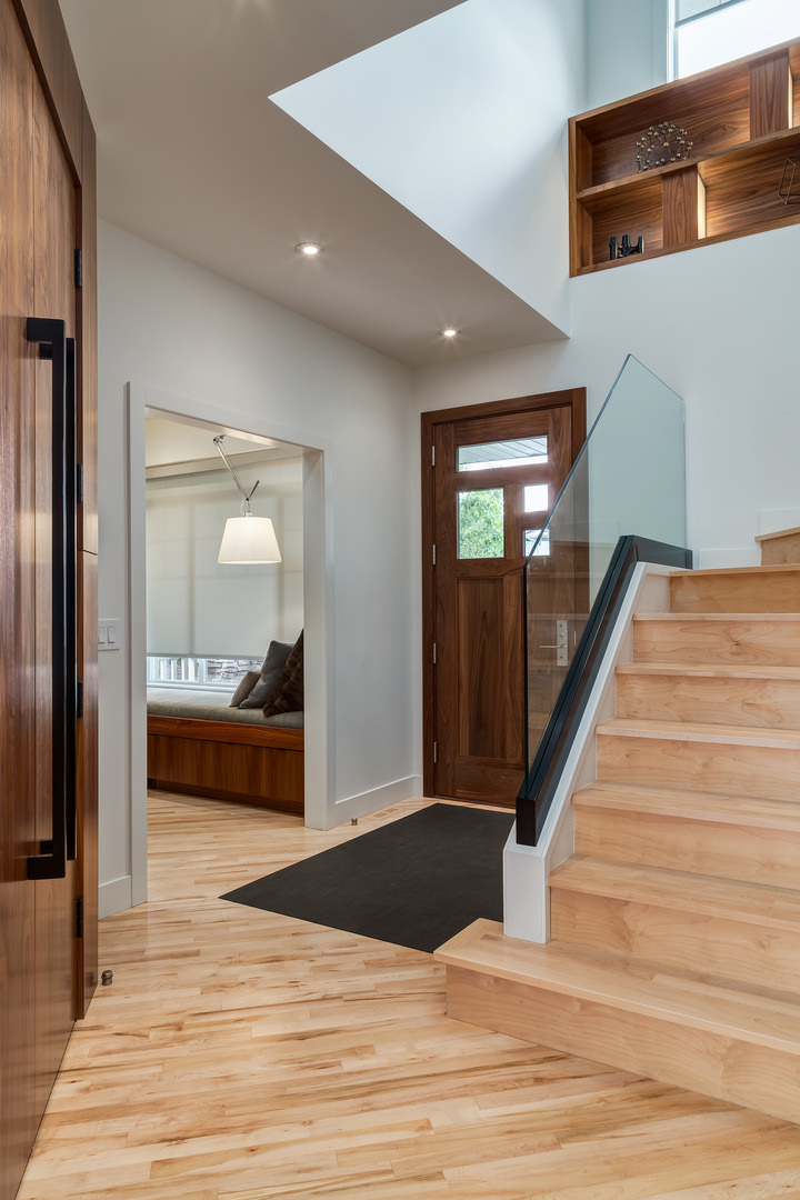 Dark wooden door with glass panels contrasts the entryway's light hardwood flooring wrapped in a black rug.