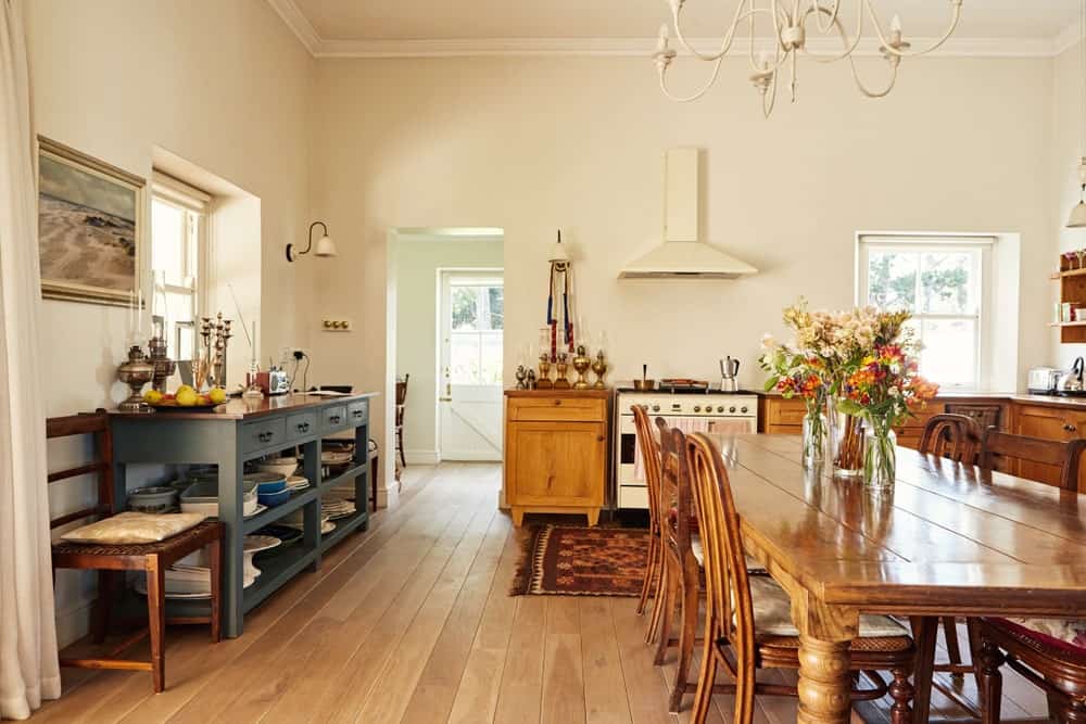 This is a cozy and homey dining area inside the cheerful beige walls and ceiling of the kitchen. This is complemented by the hardwood flooring that matches with the wooden dining table paired with wooden chairs of the same hue.