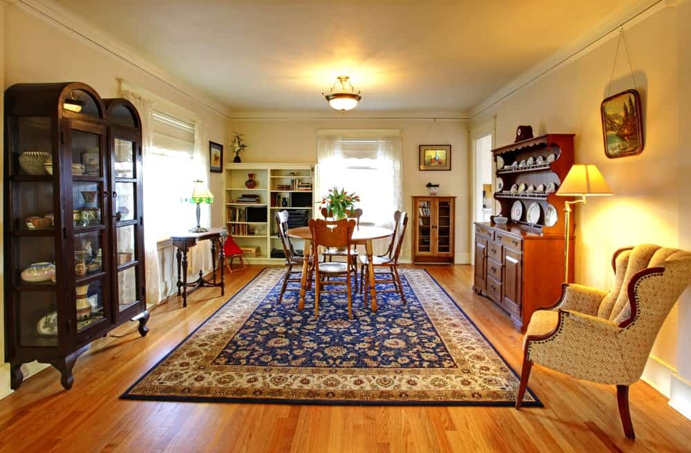 The colorful patterned area rug matches the elegance and sophistication of the dining room cabinets placed against the beige walls that complement the hardwood flooring. This matches with the wooden hue of the dining set under the semi-flush dome lighting.