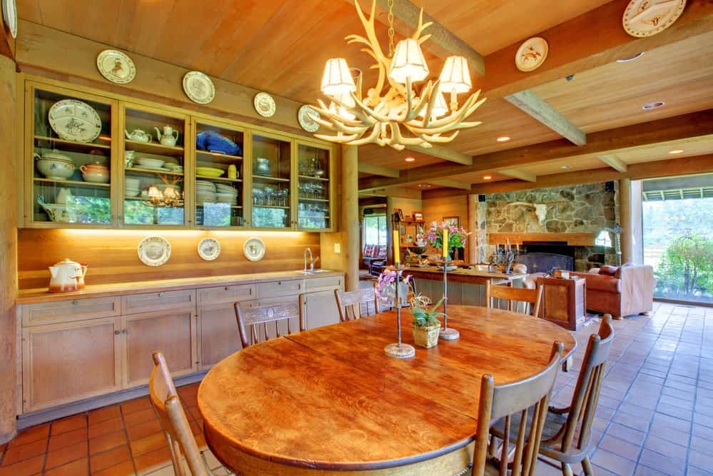 The highlight of this dining area inside the kitchen is the chandelier hanging over the elliptical wooden table. This chandelier is made of deer antlers casting off warm yellow lights onto the wooden ceiling adorned with decorative plates.