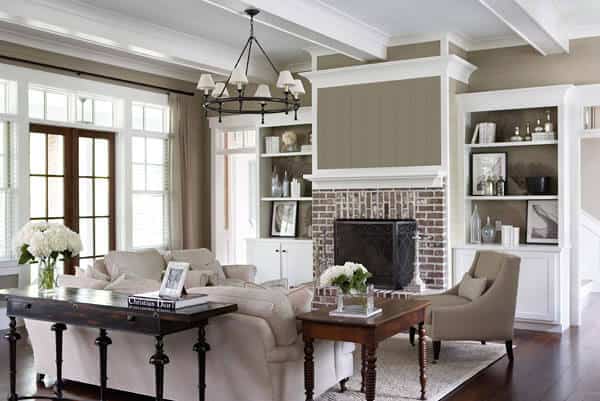 The white ceiling has exposed wooden beams with the same hue as the ceiling and the two built-in shelves that are flanking the fireplace surrounded with bricks. Across from this wall is the beige sofa set that looks comfortable and cozy.