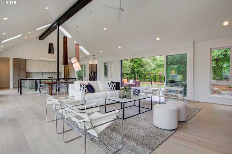 The white cathedral ceiling has a single contrasting exposed wooden beam right on the middle that supports the white ceiling fan. This matches with the white sofa, white modern armchairs and the two white round ottomans that stand out against the gray area rug.