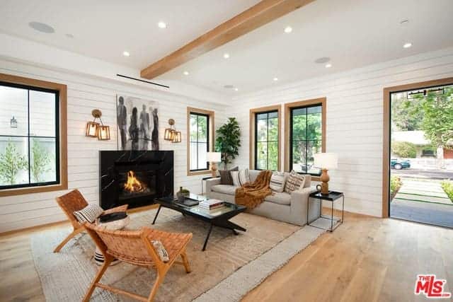 As you enter this home, you will see the living room area on the right side of the hardwood flooring that is marked with a large rustic woven area rug that matches with the light gray sofa facing a black coffee table that pairs well with the black fireplace.