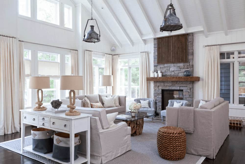 Chrome dome pendants illuminate this living room boasting skirted sofas and a glass top coffee table facing the gray tufted chairs and a brick fireplace that's lined with a wooden mantel.