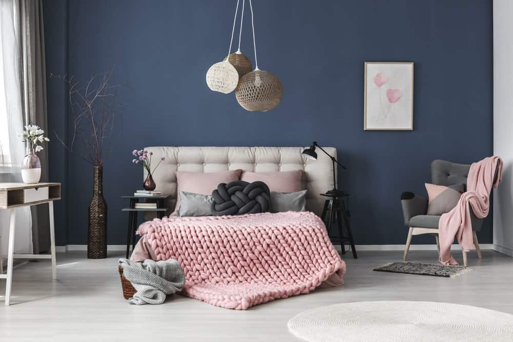 pendant lights Navy blue bedroom accented with light pink bedding, artwork and throw blanket that lays on the green tufted armchair. It is decorated with lovely flower vases and boho <a class=