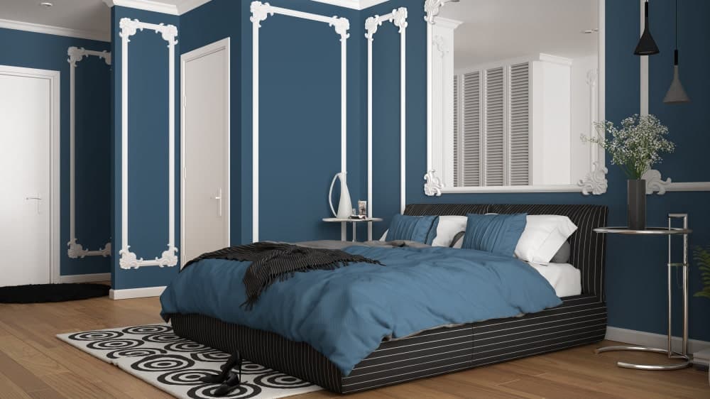 Classy primary bedroom designed with ornate wainscoting and a matching mirror that hung above the black striped bed flanked by round side tables.