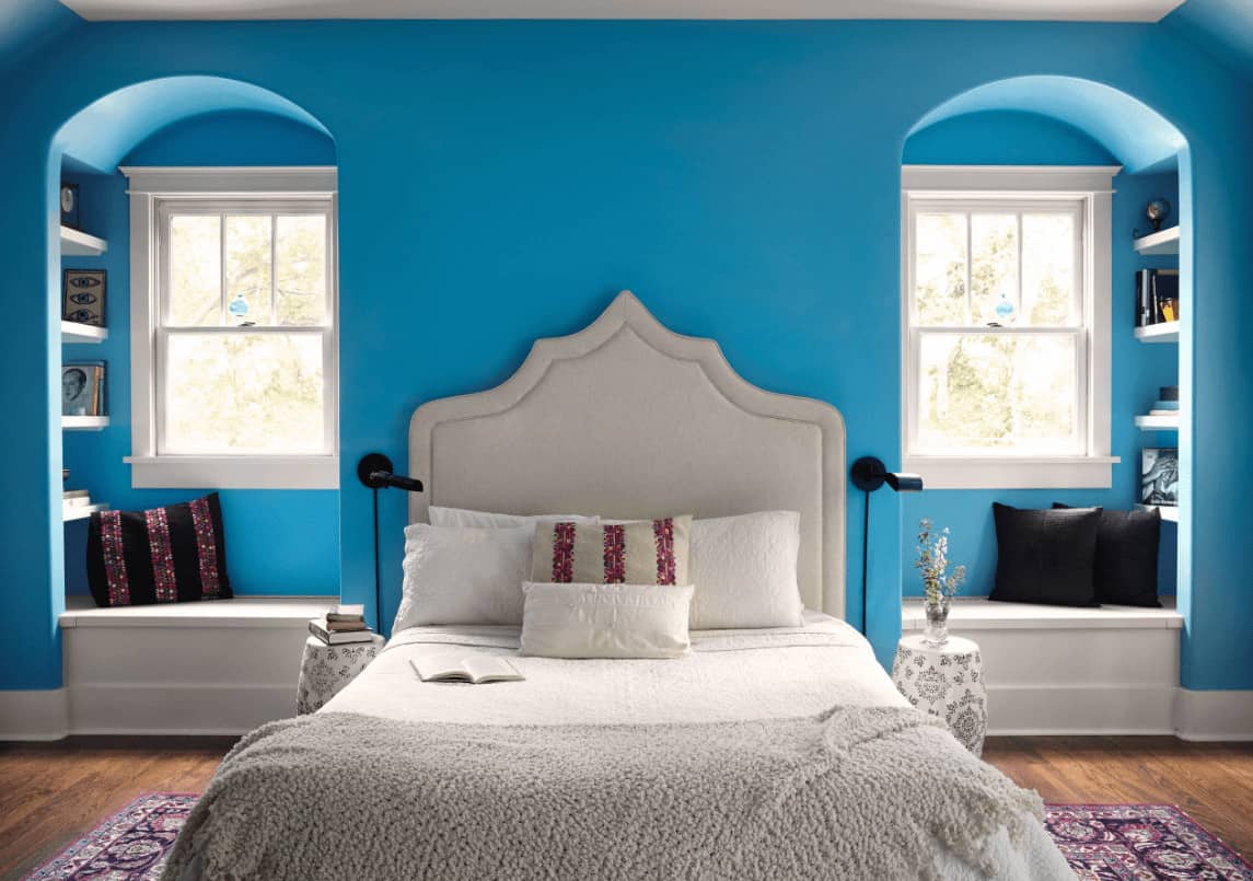 Charming bedroom with a white upholstered bed on a classic area rug along with alcove seat nooks that are completed with shelving on its sides.