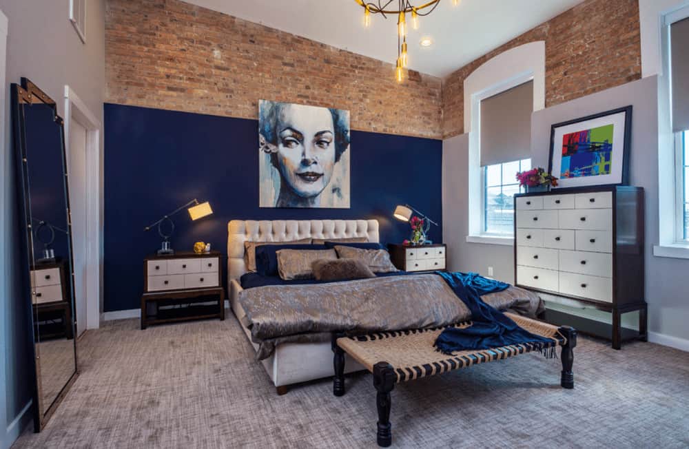 Stone brick walls add texture in this primary bedroom with a full height mirror and gray tufted bed accented by a gorgeous portrait.