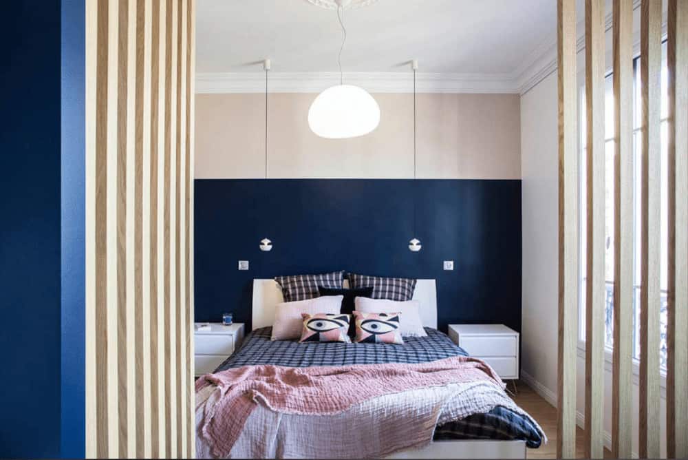 A wooden slat door opens this cozy bedroom with white nightstands and sleek bed illuminated by glass and mini pendant lights.
