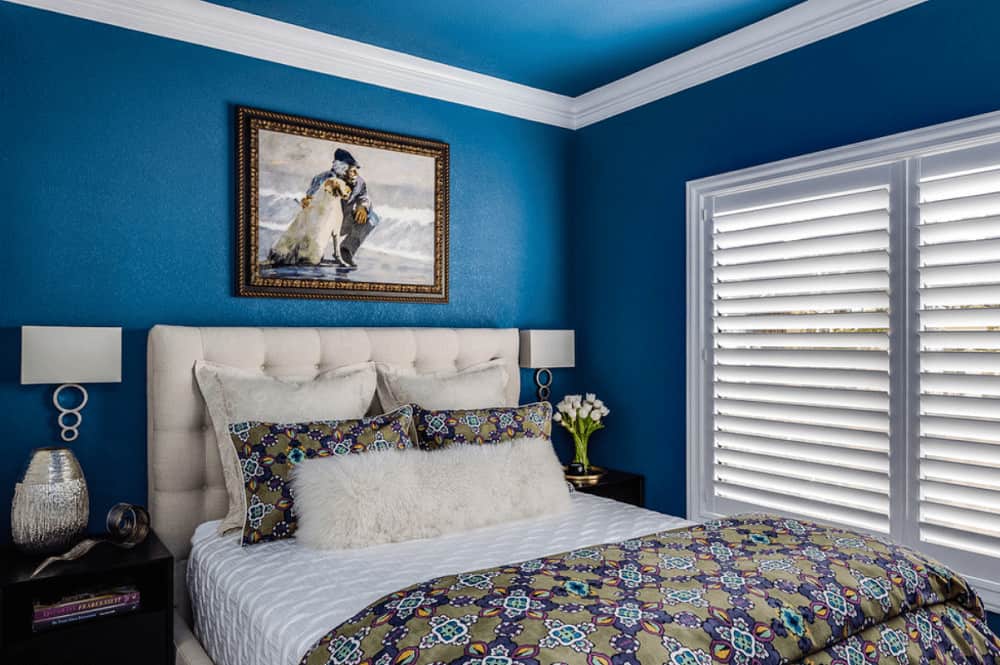 A closeup look at this blue bedroom showcasing sleek sconces above dark wood nightstands and beige tufted bed with a gorgeous painting on top.